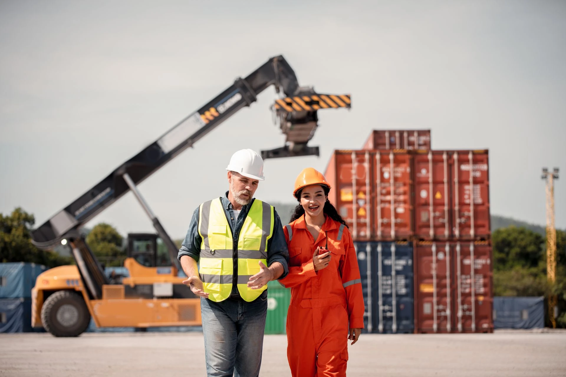 Workers at a shipping container yard with a reach stacker